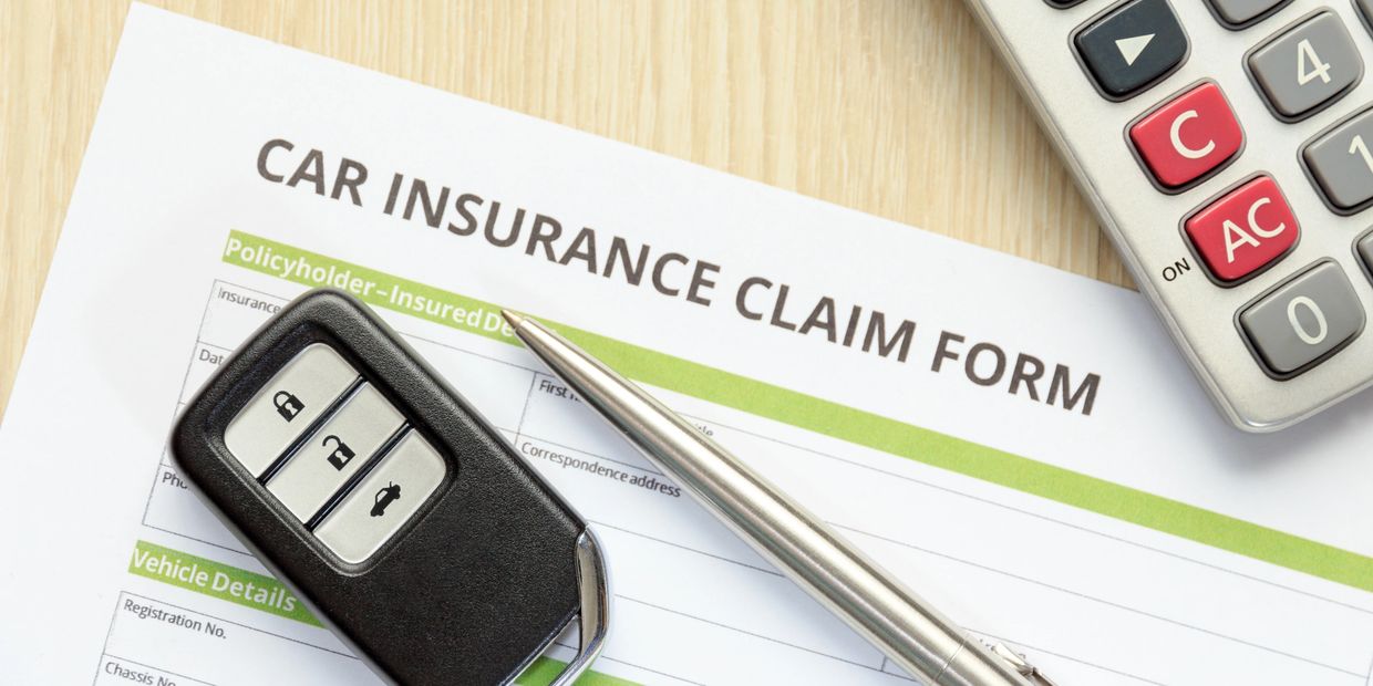 Car insurance claim form with car key, pen, and calculator on a wooden table.