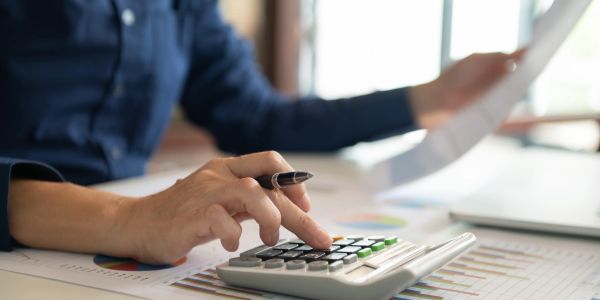 Person using a calculator while holding a document with financial charts.