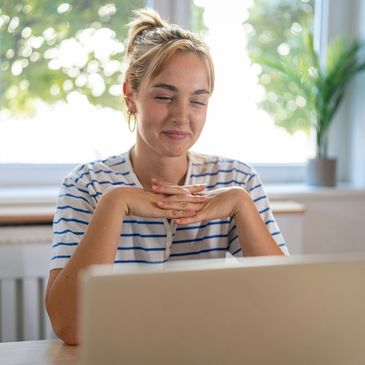 A women smiles at a laptop during an online therapy session.