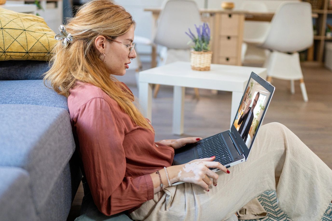 Young woman video chatting on laptop while sitting on the floor.