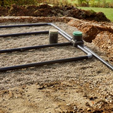 Gravel bed with black pipes and green valve covers in a dug-out area.