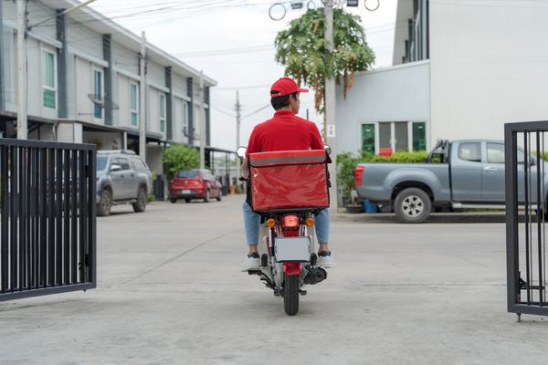 Delivery person in red uniform riding a motorbike with a delivery bag.