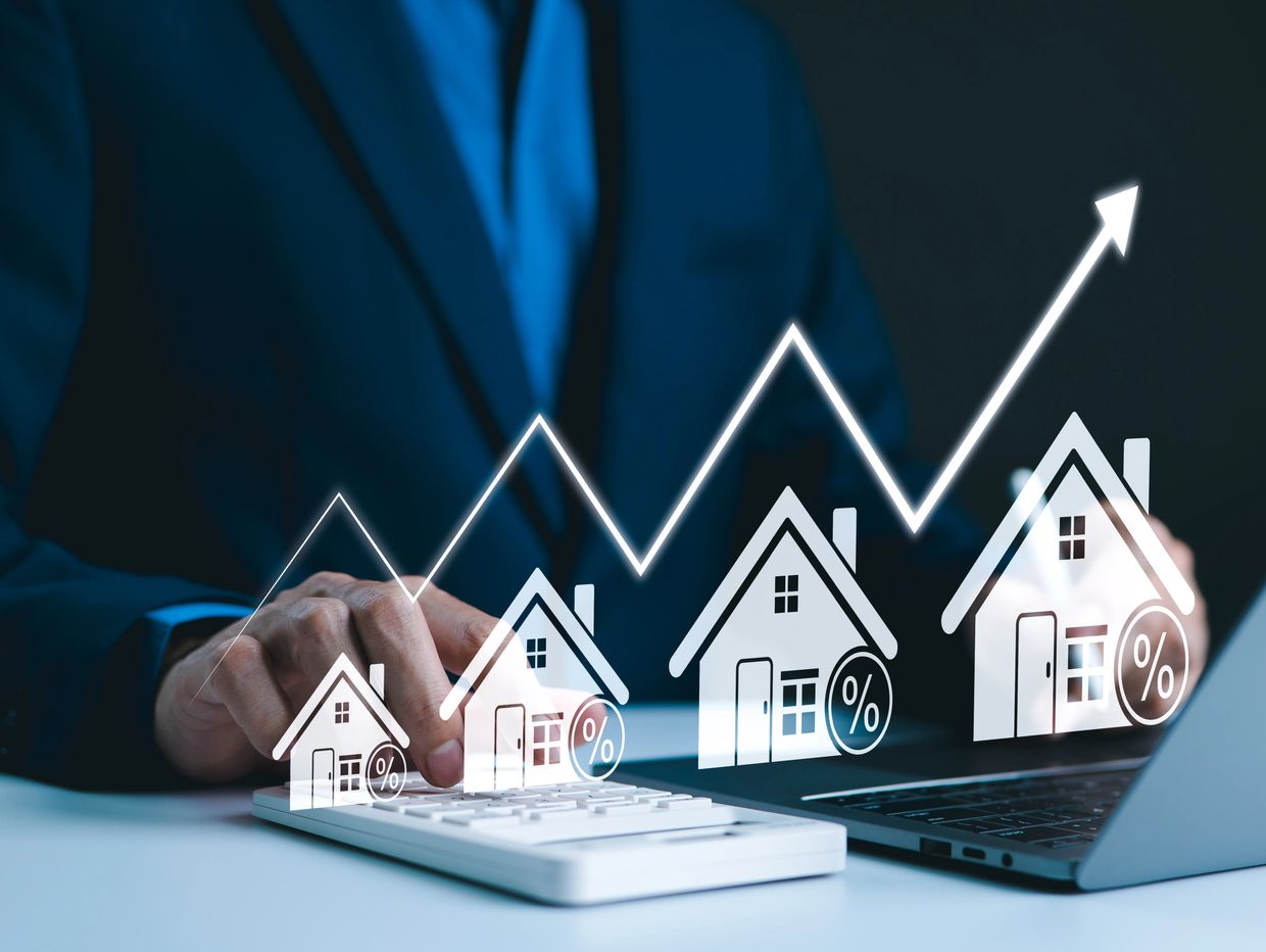 Businessman calculating rising mortgage rates with digital house icons and upward graph.