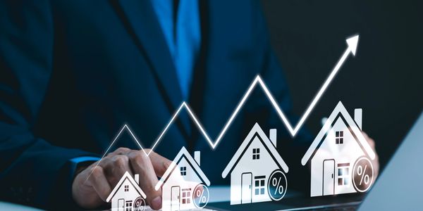 Businessman calculating rising mortgage rates with digital house icons and upward graph.