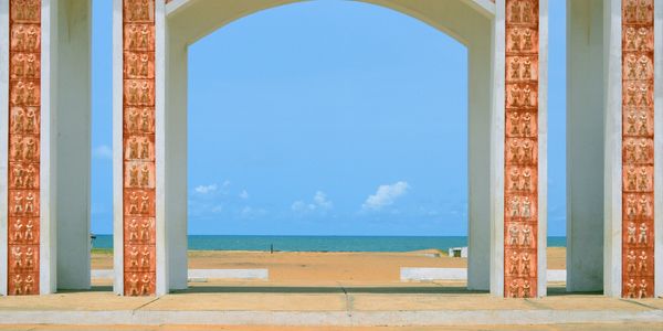 Arched structure framing a sandy beach and ocean under a clear blue sky.