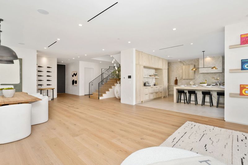 Modern open-plan living area featuring wooden floors, a dining table, and a kitchen with island seating and contemporary decor.