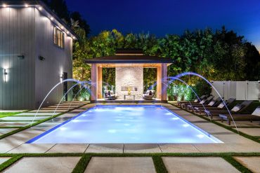 Modern outdoor pool with water fountains at night.