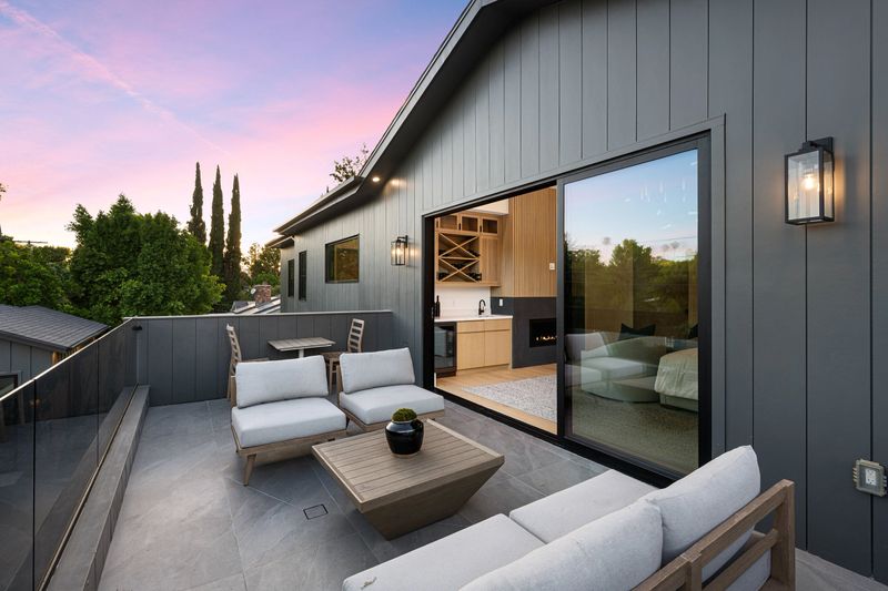Modern outdoor patio with comfortable seating, glass railing, and sliding doors leading to a stylish interior at sunset.