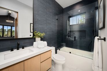 Modern bathroom with black tiled shower and wooden vanity.