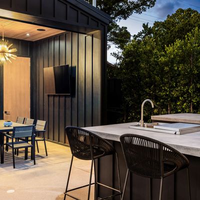 Modern outdoor kitchen and dining area with sleek black furniture and ambient lighting.
