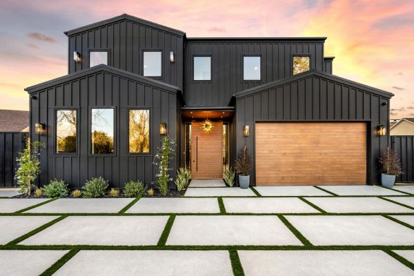 Modern black house with wooden accents and geometric driveway at sunset.