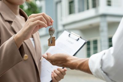 Real estate agent handing over house keys with contract in background.