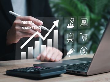 Person drawing an upward graph labeled Digital Marketing with marketing icons on a transparent screen.