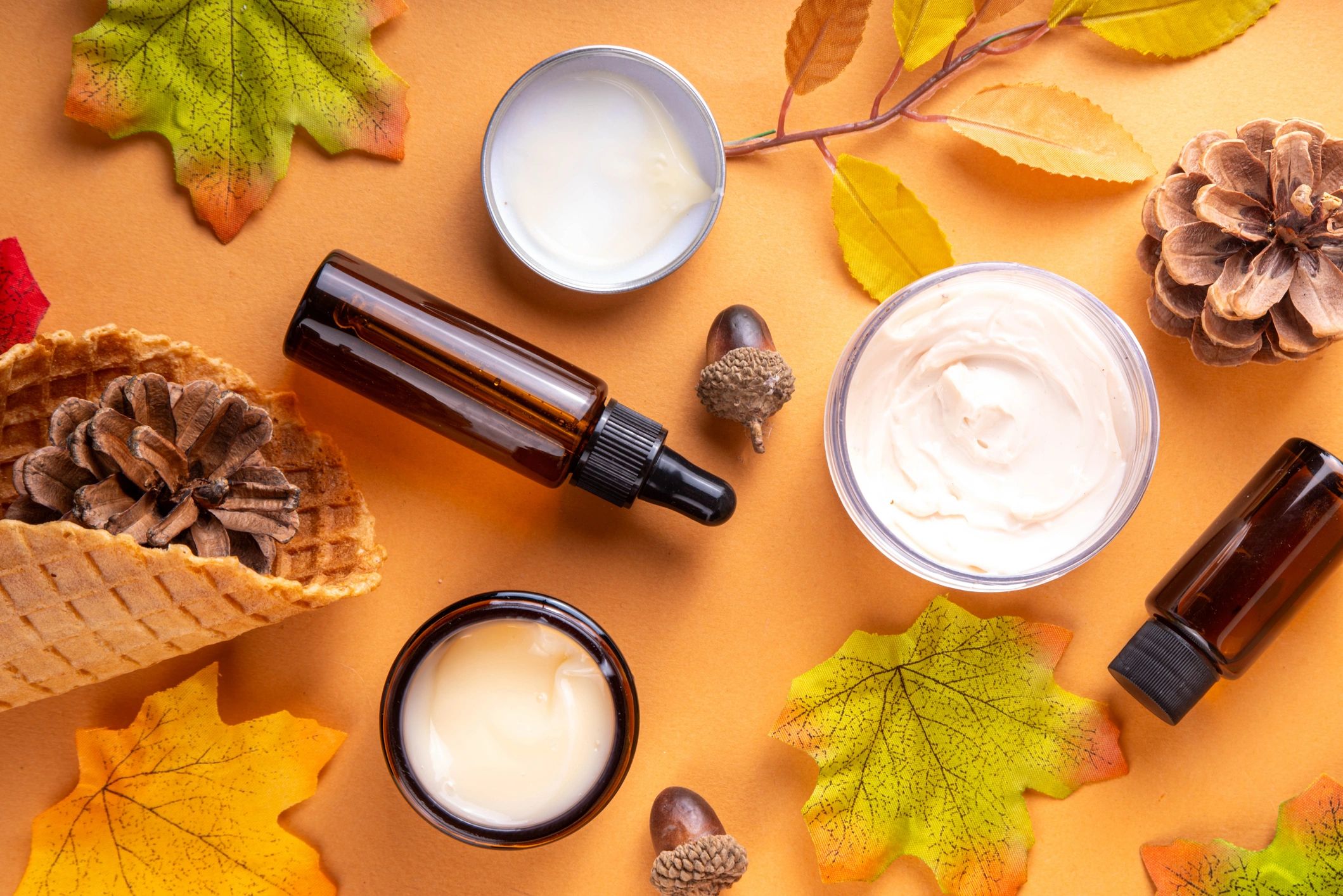 Autumn-themed skincare products with leaves, cones, and acorns on an orange background.