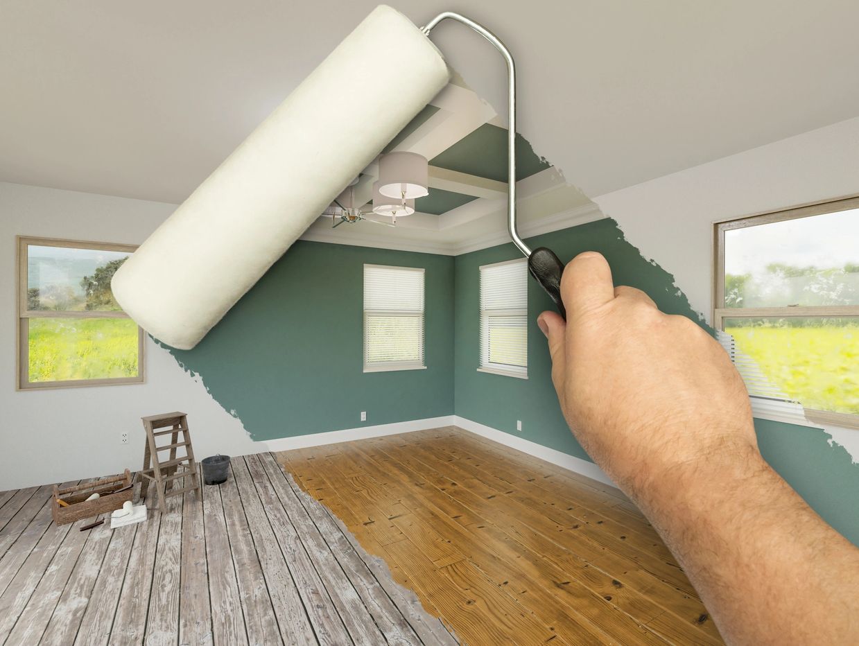 A hand painting a green wall white with a roller in a bright room.