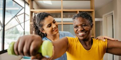 Woman helping senior woman exercise with dumbbells.