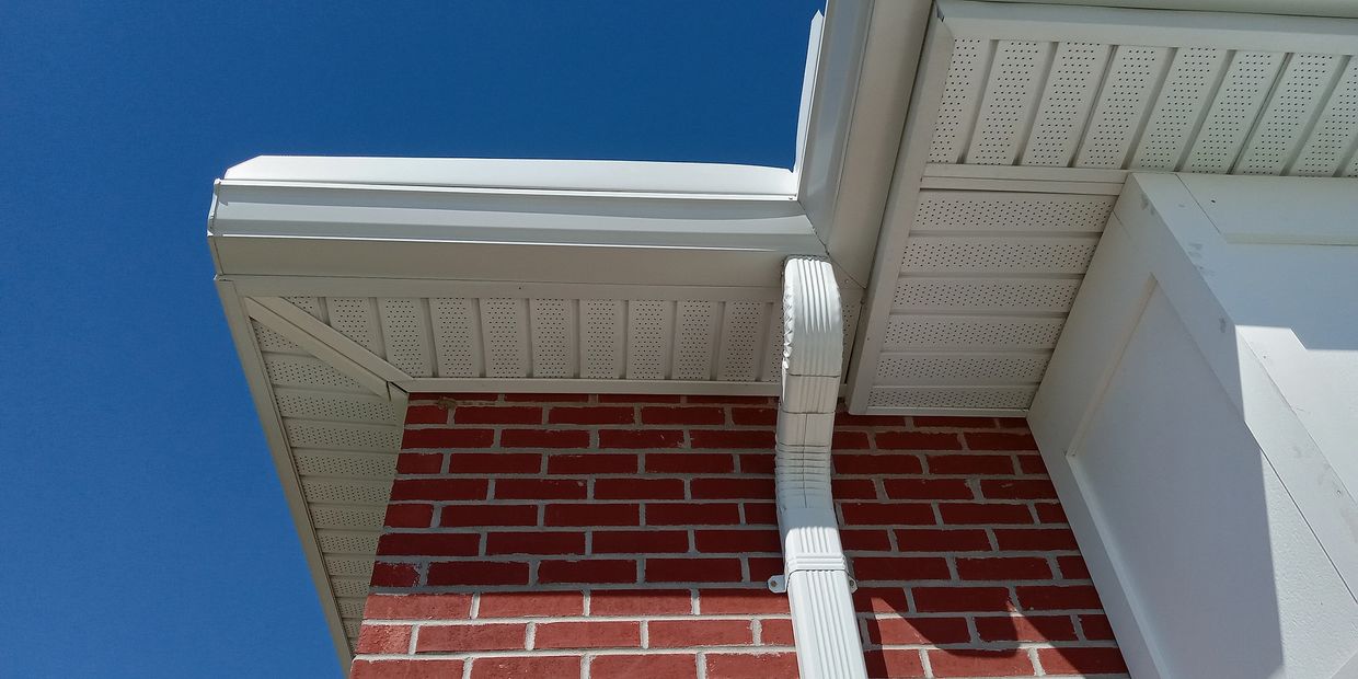 Close-up of a white gutter system on a red brick house against a clear blue sky.