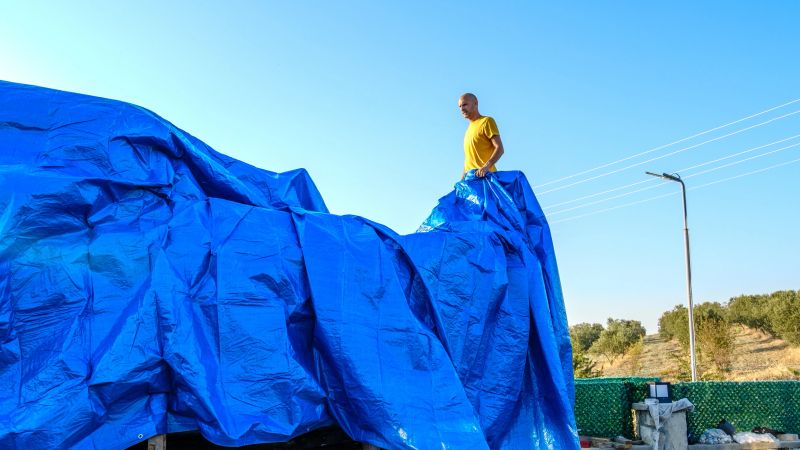 A middle-aged man covering his boat on land with a blue tarp