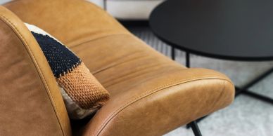 Close-up of a tan leather chair with a cushion and black round table.