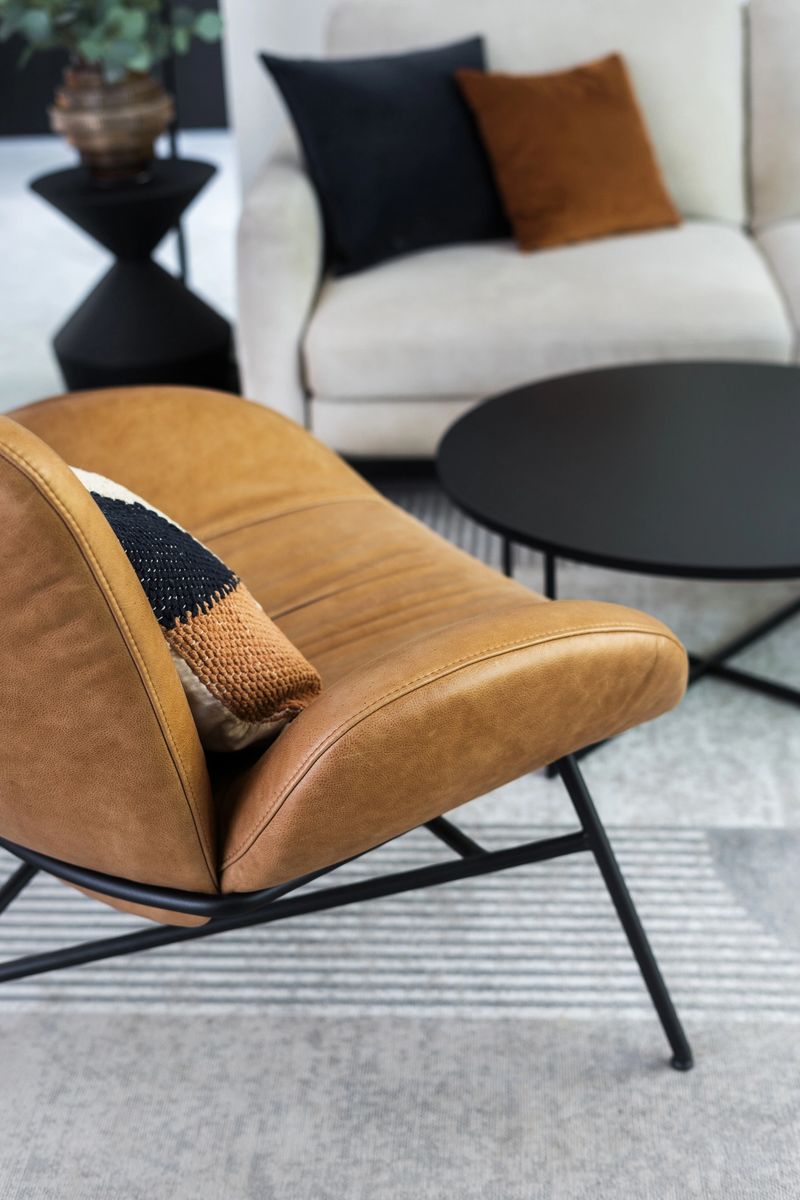 A warm, inviting living room features a sleek leather chair with a decorative pillow, a circular coffee table, and minimalist decor creating a stylish atmosphere for relaxation at home