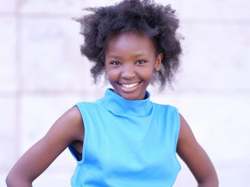 Smiling girl in a blue sleeveless top and jeans with hands on hips.