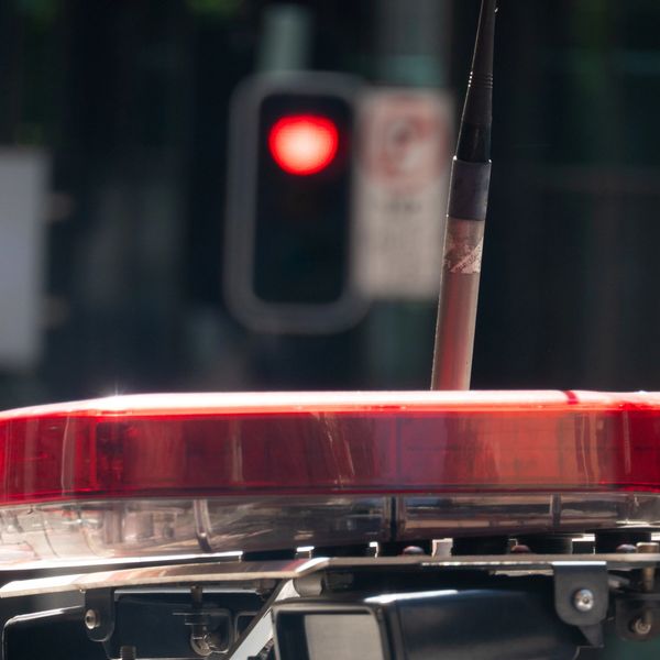 Close-up of a police car's red emergency light bar with a red traffic light in the background.