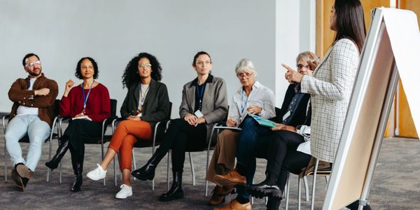 A woman presenting to a seated group in a conference room with a flip chart.