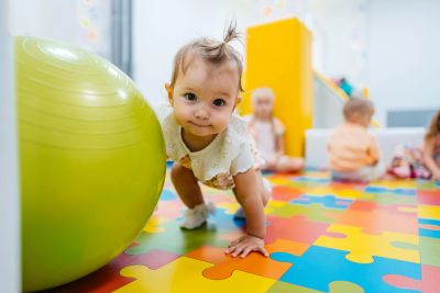 Baby crawling near a large green ball on a colorful puzzle mat.