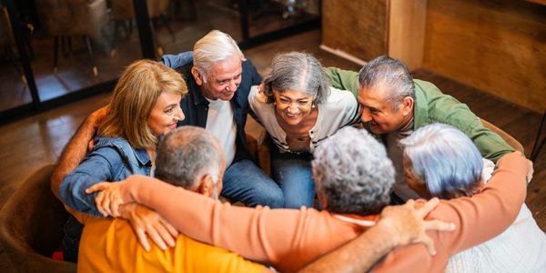A group of elderly friends smiling and hugging in a circle.