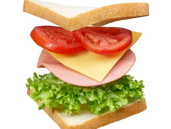 A fresh sandwich with lettuce, ham, cheese, and tomato between white bread slices.