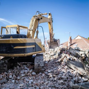 Yellow excavator clearing debris from demolished building site.