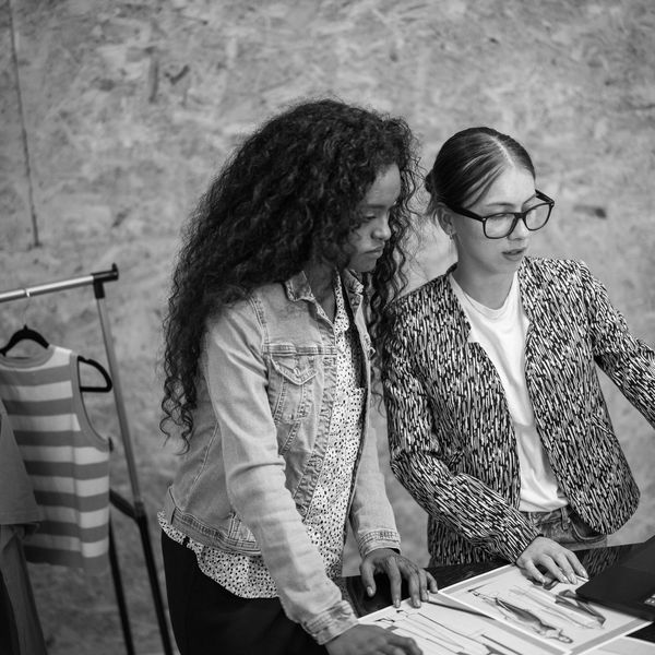 Two women collaborating over fashion sketches in a studio.