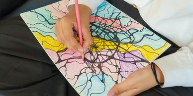 Person coloring an abstract design with a pink pencil on paper.
