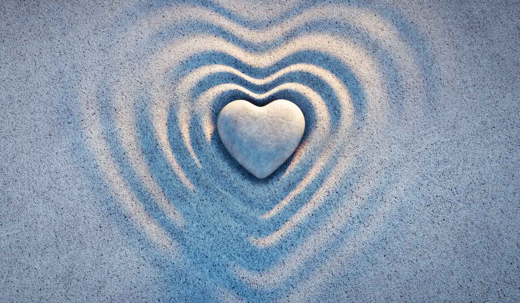 Heart-shaped stone with ripples in sand forming heart patterns.