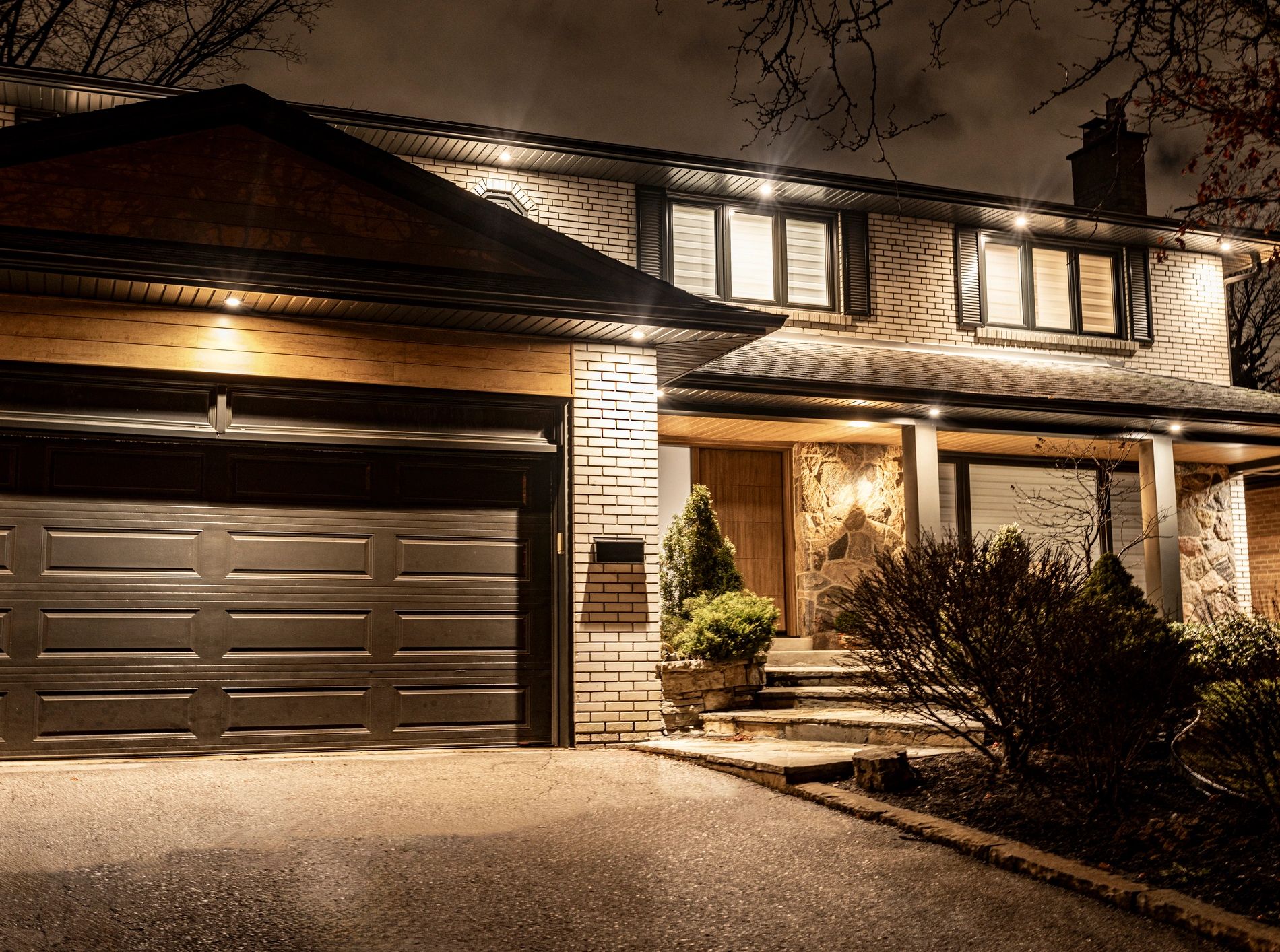 Exterior view of a well-lit house and garage at night.