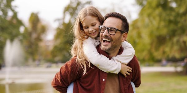 A joyful father giving his daughter a piggyback ride in the park.
