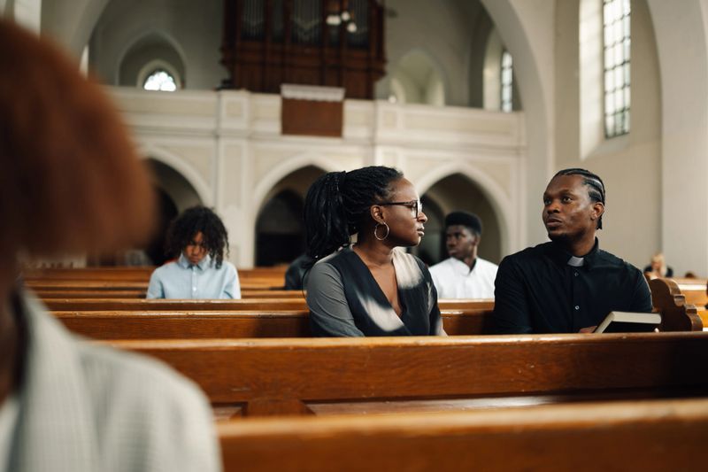 Young woman is receiving guidance and support from a priest inside a church, engaging in a meaningful conversation about faith and spirituality