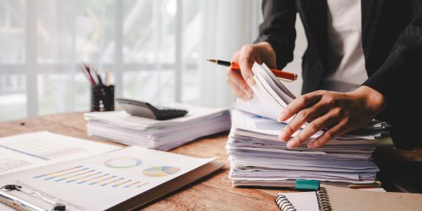 Person organizing stacks of papers and documents on a wooden desk.