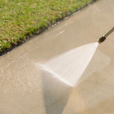 A pressure washer cleaning a concrete sidewalk near grass.