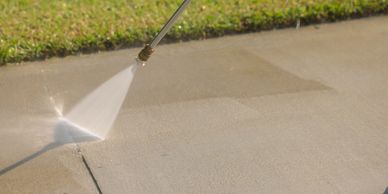 Pressure washer cleaning a concrete sidewalk near grass.