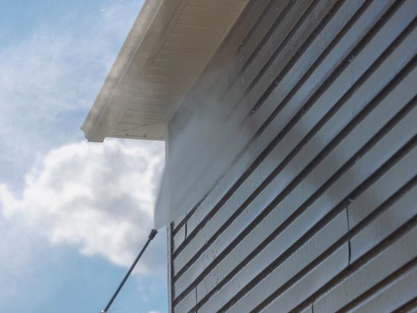 Pressure washing the side of a house on a sunny day.
