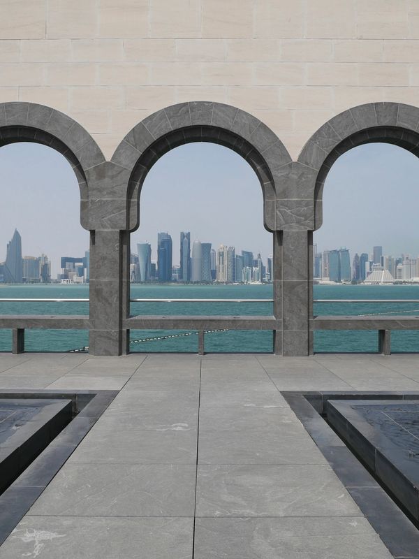 Three arched windows frame a city skyline across turquoise water.