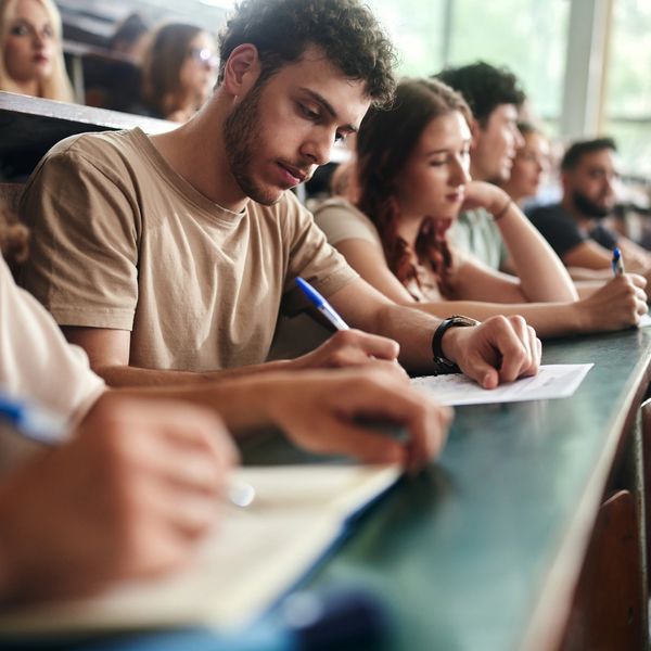 Students attentively taking notes in a university lecture hall.