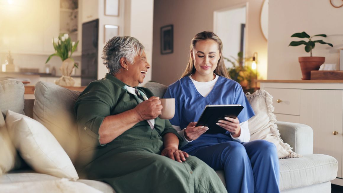 Caregiver and elderly woman sharing a joyful moment on the couch.