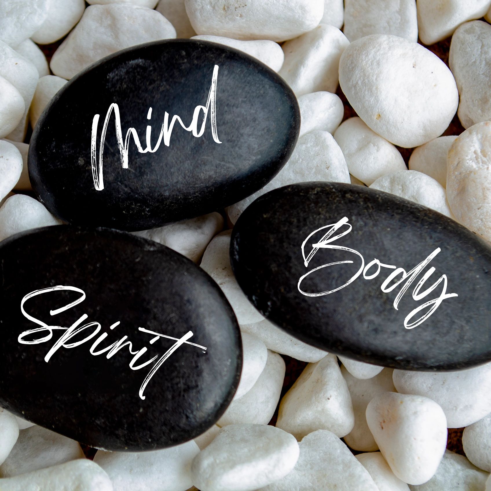 Three black stones labeled Mind, Body, Spirit on white pebbles.