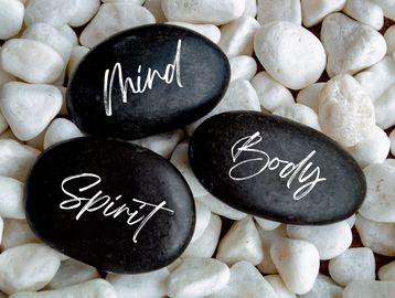 Black stones labeled Mind, Body, Spirit on white pebbles.