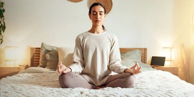 Woman meditating peacefully on a bed in a cozy bedroom.