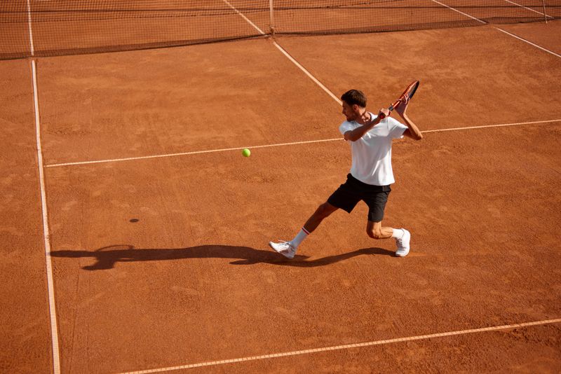 Dynamic image of athletic young man, tennis player in motion on court, playing, practicing, hitting ball with racket. Focus. Concept of sport, competition, game, hobby, active and healthy lifestyle