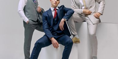 Three men in stylish suits posing confidently against a minimalistic background.