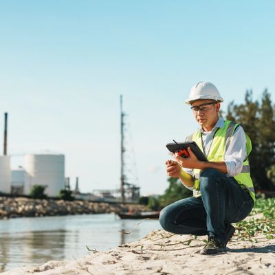 Engineer in safety gear inspecting industrial site by water.